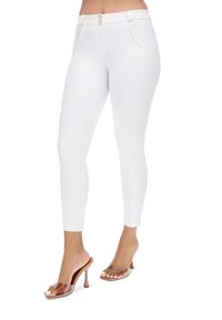 Pantalon blanc ajusté avec une texture lisse, fermeture à deux boutons et poches latérales, associé à des sandales à talons transparents.