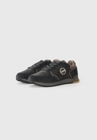 Svart ruskinn sneakers med teksturert finish, beige detaljer, rund logo-patch og gummisåle. Snøring med forsterket tå.