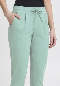 Ljus mintgröna joggers i mjukt tyg, med dragsko i midjan, sidofickor och veckad frontdetalj.