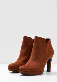 Stivali alla caviglia in suede marrone con punta arrotondata, tacco a stiletto alto, texture liscia e design minimalista.