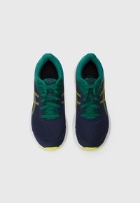 Baskets de sport bleu marine avec des accents verts, dessus en maille et semelle blanche. Présente des lacets verts et de subtils détails jaunes sur les côtés.