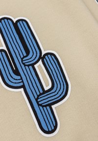 Beige stof met een zwart en blauw geborduurd cactusontwerp, met duidelijke verticale lijnen en omlijnd in het wit.