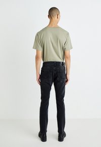 Vyriška alyvuogių žalia marškinėliai ir juodi džinsai. Marškiniai su apvaliu iškirpimu; džinsai turi užpakalinius kišenes ir liekną dizainą.