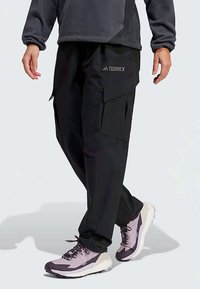 Svarte cargobukser med flere lommer, skreddersydd passform og slitesterkt stoff, kombinert med lette grå og lilla tursko.