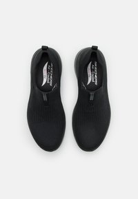 Zapatillas negras de tipo slip-on con una parte superior de punto transpirable, superficie texturizada y una lengüeta en el talón. Incluyen una plantilla acolchada para mayor soporte.