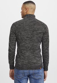 Musta ja harmaa sekoitetti turtleneck-neule, jossa on tiukka muotoilu, ribbireunat hihansuissa ja helmassa; puuvillasekoitteen materiaali. Takakatsaus, jossa on tuotelapun yksityiskohta.
