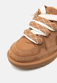 Baskets en daim marron avec des détails en maille, dotées de lacets épais en blanc et marron à motifs, d'un col rembourré et d'une semelle en caoutchouc texturé.