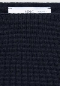 Tissu en tricot côtelé bleu marine foncé avec une étiquette de vêtement blanche partiellement visible présentant le nom de la marque "MNG".