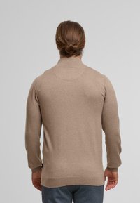 Maglione beige lavorato a maglia con maniche lunghe, colletto alto e rifiniture a costine sui polsi e sull'orlo. Tessuto morbido con una finitura liscia.