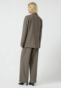 Bruin op maat gemaakt kostuum met een lange blazer met gestructureerde schouders en brede pijpen. Glad stof met een subtiele textuur.