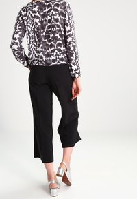 Pantaloni neri a vita alta abbinati a una maglietta grigia e nera con motivo, a maniche lunghe e dalla vestibilità ampia. Scarpe con tacco in satin argentato completano il look.