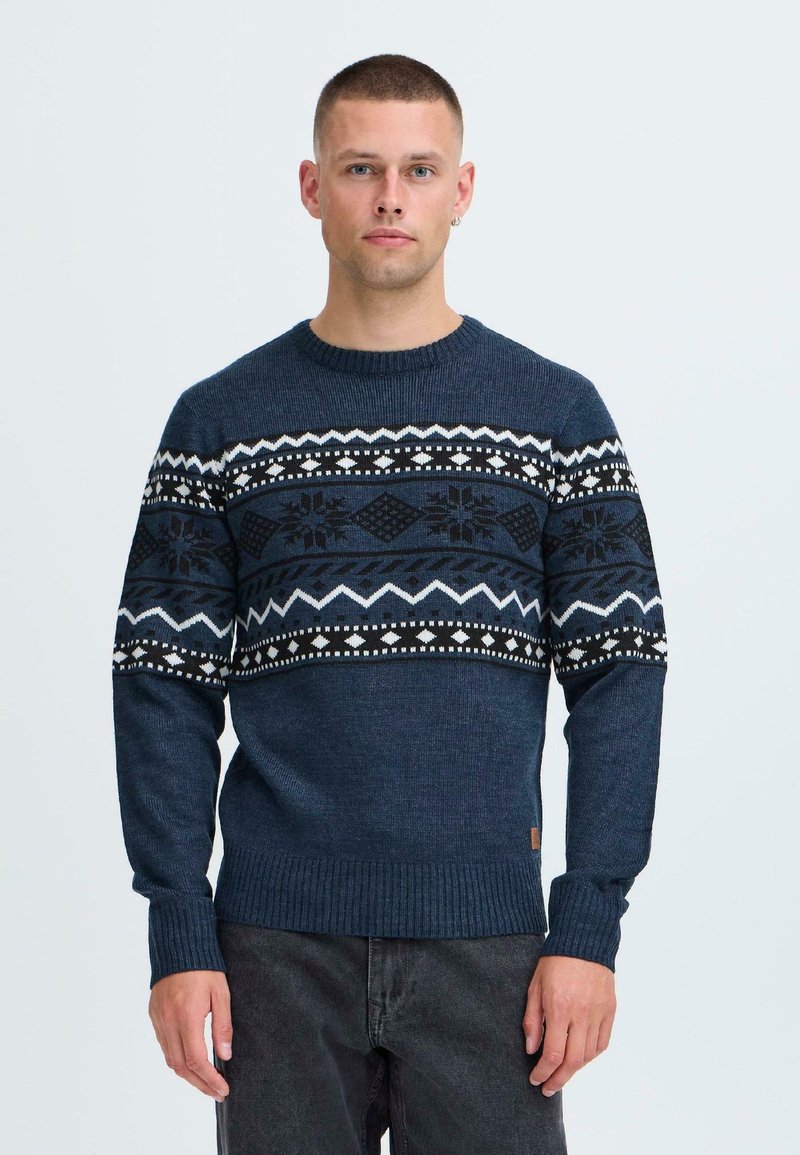 Pulover tricotat navy cu un model geometric în alb și negru pe piept, cu manșete și tiv ondulate. Material dintr-un amestec de bumbac.