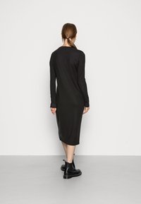 Svart långärmad klänning i knälängd med en åtsittande siluett och mjuk textur. Bärs med svarta ankelskorn, som visar upp en minimalistisk design.