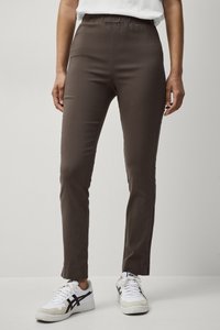 Pantalons marron ajustés avec une taille élastique et une texture lisse. Associés à des baskets blanches avec des détails noirs.