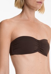 Brossi bandeau bikinitop z nabranimi šivi, gladko teksturo in brez naramnic, primeren za kopalke. Dodatne opreme ni vidne.