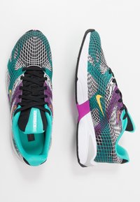 Idrottsskor med ovandel i nät i turkos, svart och lila. Har en vit sula, gula accenter och ett mönstrat design.