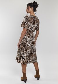 Kleid mit Leopardenmuster, kurzen Ärmeln, gebundenem Taillengürtel und weit ausgestelltem Saum. Hergestellt aus glattem Stoff in Brauntönen mit schwarzen Akzenten.