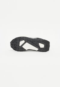 Semelle de chaussure de sport noire avec un caoutchouc texturé pour l'adhérence, dotée d'un accent blanc cassé et de motifs géométriques pour des éléments de design supplémentaires.
