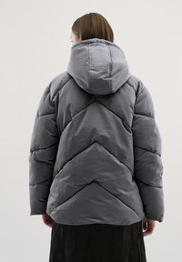 Grijze pufferjack met capuchon, voorzien van een doorgestikt chevronpatroon, zachte textuur en een ontspannen pasvorm, ontworpen voor warmte en comfort.