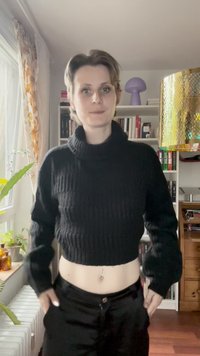 Schwarzer, gerippter Rollkragen-Crop-Pullover mit langen Ärmeln, kombiniert mit hoch taillierten schwarzen Hosen. Im Hintergrund sind Bücherregale und Pflanzen zu sehen.