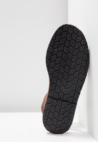 Vue de dessous d'une chaussure marron montrant une semelle en caoutchouc noire avec un motif de bande de roulement hexagonal irrégulier texturé.