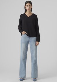 Blusa nera a maniche lunghe con scollo a V abbinata a jeans a gamba larga azzurri e tacchi blu, caratterizzata da una vestibilità rilassata e una trama sottile.