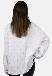 Witte oversized pullover met kleine roze hartjespatronen, gemaakt van een gestructureerde stof met zijsplitten en losse mouwen.