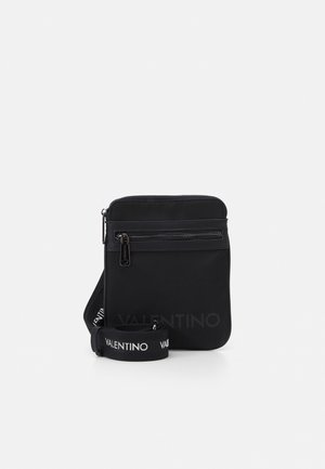 Bolso bandolera negro compacto con bolsillo delantero con cremallera, correa negra con la palabra "VALENTINO" en letras blancas mayúsculas.