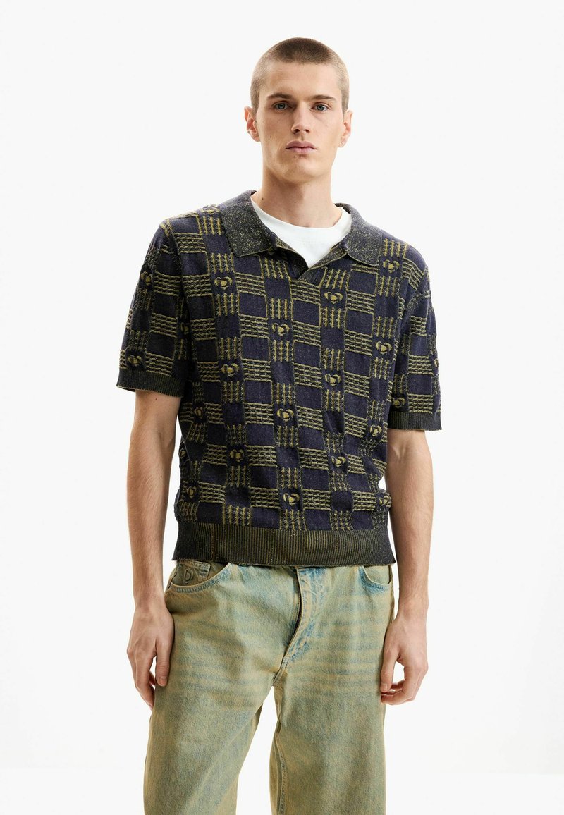 Polo à manches courtes en maille bleu marine avec motif damier vert olive. Caractérisé par un col uni et un ourlet côtelé. Porté avec un jean bleu clair.