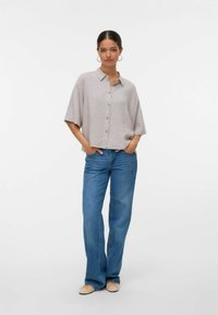 Chemise à manches courtes gris clair, coupe décontractée, associée à un jean large bleu et des ballerines beiges. Design simple, lignes épurées, look décontracté.