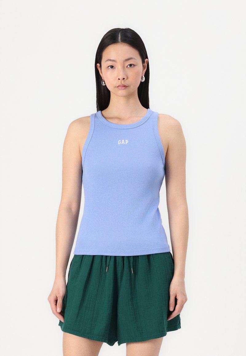 Ljusblå ribbad linne med rund halsringning och GAP-logotyp i vitt; kombinerat med gröna veckade shorts. Slät textur, åtsittande design.