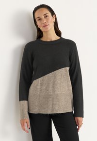 Pullover mit einem schwarzen oberen Bereich und einem beigen unteren Bereich, der diagonal geteilt ist, Rippbund und langen Ärmeln. Weiche Textur.