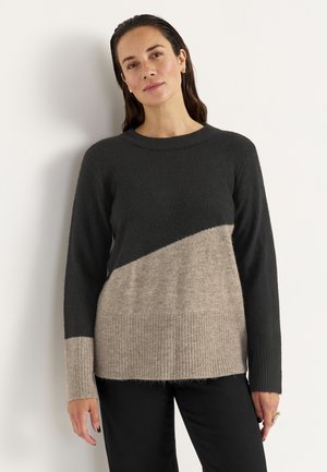 Trui met een zwart bovenstuk en een beige onderstuk met een diagonale scheiding, ribbelachtige onderrand en lange mouwen. Zachte textuur.