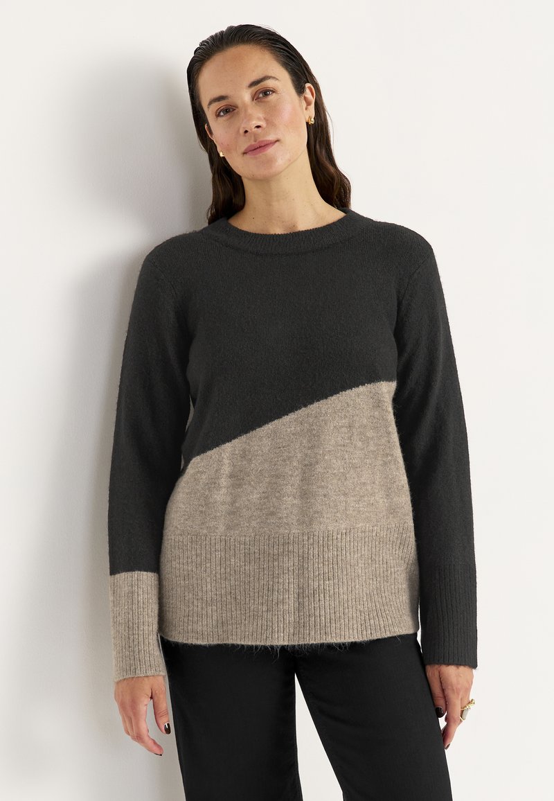 Pullover mit einem schwarzen oberen Bereich und einem beigen unteren Bereich, der diagonal geteilt ist, Rippbund und langen Ärmeln. Weiche Textur.