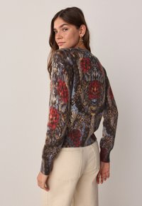 Džemper u smeđoj boji s crvenim i plavim cvjetnim i leopard uzorcima. Ima duge rukave, rebraste manžete i dizajn uskog struka.