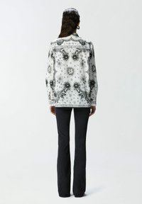 Blusa bianca con motivi floreali e paisley neri, maniche lunghe, colletto e vestibilità rilassata, abbinata a pantaloni neri a zampa.