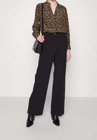 Black wide-leg trousers paired with a brown patterned blouse. The blouse has a collar and long sleeves, featuring a shiny texture. Accessorized with a small black handbag.