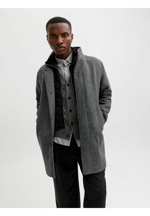 Grijs wollen blend jas met een hoge kraag, voorzien van een knoopsluiting en een zwarte gevoerde binnenvoering over een grijs vest en gestreept shirt.