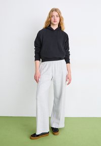Zwarte cropped hoodie met een capuchon, gecombineerd met lichtgrijze wijde sweatpants en zwarte sneakers met bruine zolen. Eenvoudig ontwerp, casual stijl.