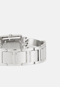 Silver metal watch with a linked bracelet design. Features rectangular and square links, engraved "GUESS" logo on select links.