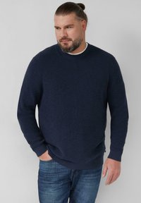 Granatowy sweter dziany o fakturowanym wzorze, z okrągłym dekoltem oraz ściągaczami na rękawach i u dołu. Zestawiony z niebieskimi dżinsami dla uzyskania swobodnego wyglądu.