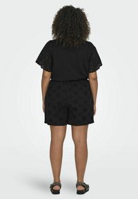 Crna majica s kratkim, vezivanim rukavima i labave crne kratke hlače s cvjetnim uzorkom. Jednostavan dizajn, uparen s ravnim sandalama.