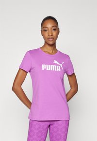 Violetinis medvilninis marškinėlis su trumpomis rankovėmis ir apykakle, kuriame yra didelis baltas "PUMA" logotipas ir mažas Puma katės grafikas.