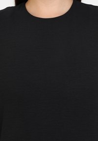 Musta crewneck-paita, joka on valmistettu sileästä kankaasta ja jossa on yksinkertainen muotoilu sekä rento istuvuus. Lyhyet hihat, minimalistinen tyyli ja tekstuuri.