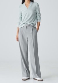 Ljust blå, ribbad tröja med V-ringning och lång ärm, tillsammans med högmidjade grå, veckade byxor. Vita sneakers fullbordar outfiten.