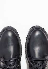 Chaussures en cuir noir à bouts ronds, surface texturée, design à lacets et coutures contrastées le long des bords.
