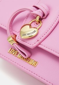 Růžová kožená kabelka s kultivovaným zlatým přívěskem ve tvaru srdce a značkou "LOVE MOSCHINO" na přední straně. Hladký povrch s prošívanými detaily.