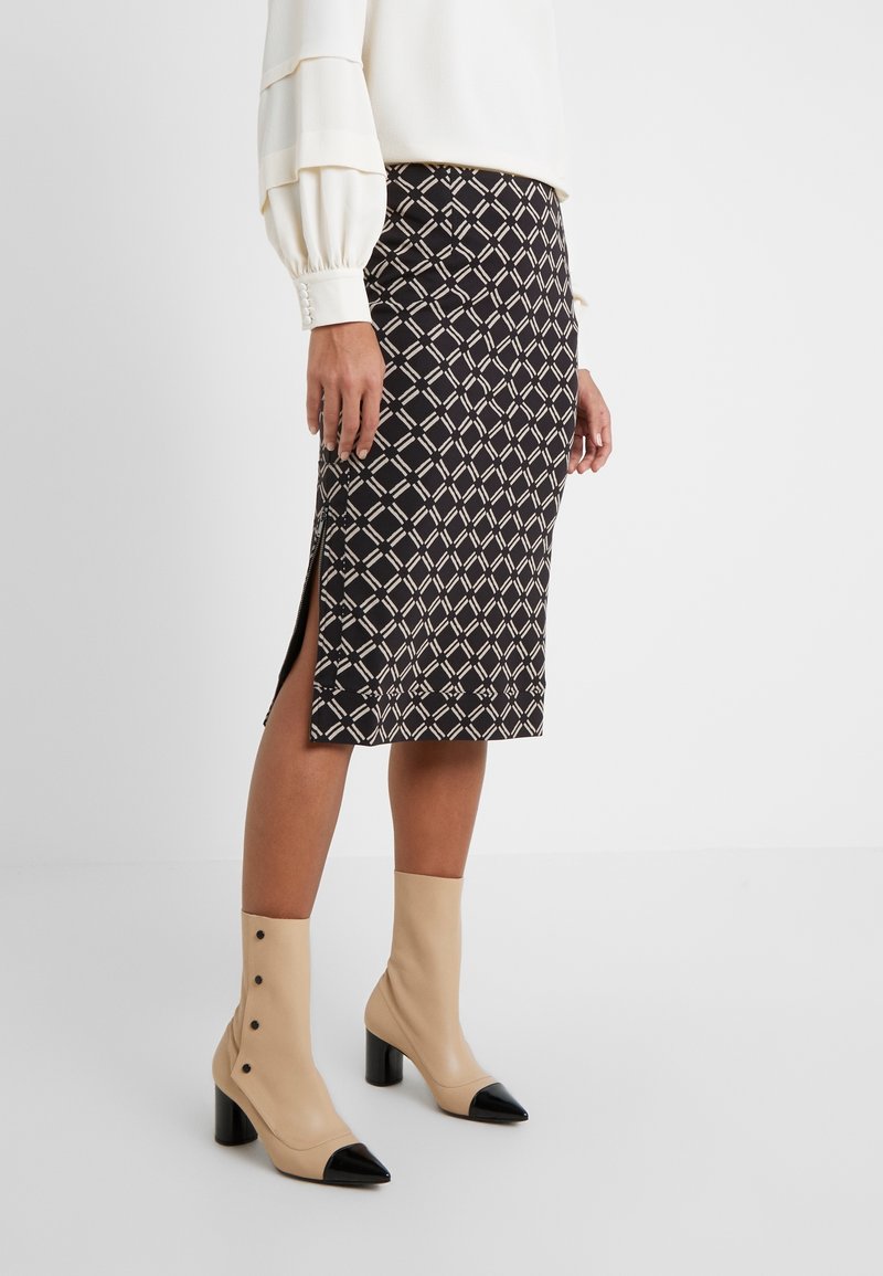 Kvinde iført en sort og beige ternet midinederdel med sidespalte, hvid bluse og beige ankelstøvler med sorte tåhætte og knapper.