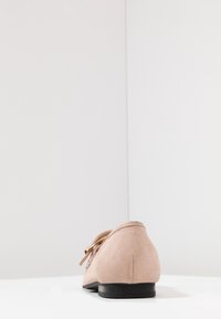 Lichtroze suède schoen met een afgeronde neus, zwarte platte zool en een decoratieve strikdetail. Gladde textuur en minimalistisch ontwerp.