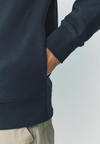 Marineblauwe sweatshirt met geribbelde manchetten en zoom. Voorzien van zijzakken, gladde textuur en gestikte details langs de naden.